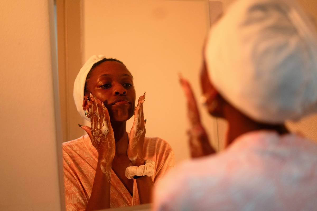 Woman applying drugstore concealer with clean brushes; budget skincare tip visible in mirror reflection
